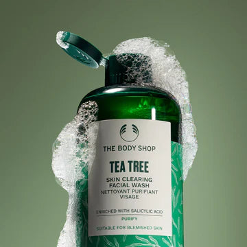 Bottle of The Body Shop's Tea Tree facial wash with an open cap and foam running down the sides