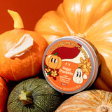 Container of The Body Shop's Sugar Pumpkin body butter surrounded by pumpkins on an red background